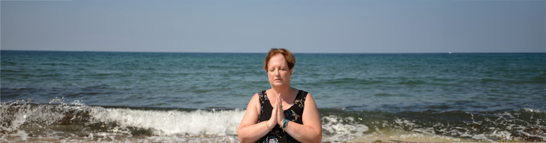 אישה יושבת על שפת הים ידיה צמודות לפני הגוף